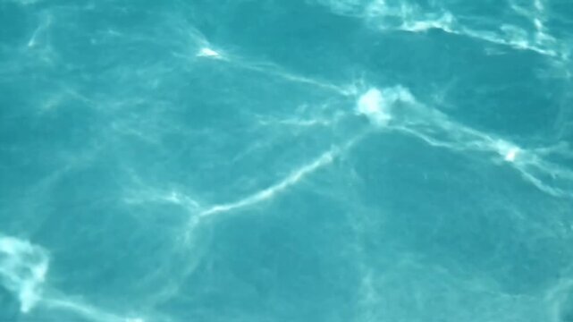 Sunlight caustics shimmering on blue swimming pool water surface.