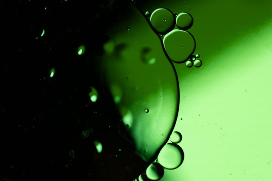 Green liquid bubbles drifting through dark abstract fluid with glowing macro backlight