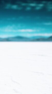 A wide view shows snow covering the ground. Distant mountains appear against a cloudy sky. The scene is bright and clear, with shades of blue in the sky.