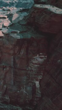 A group of people stands close to a rocky cliff during daylight. They look at the rock formations and enjoy the surroundings. Some are taking pictures while others talk.