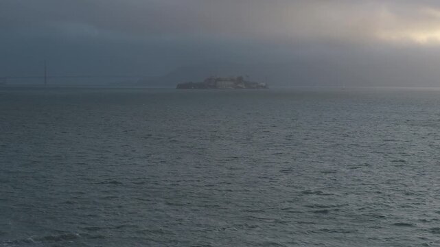 Mist covered alcatraz island over choppy waves of San Francisco Bay - wide, aerial shot