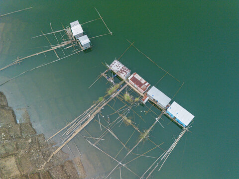 Aerial view of floating fish farm structures made of bamboo and metal on the calm green water of Wadaslintang Reservoir in Wadaslintang, Central Java, Indonesia.