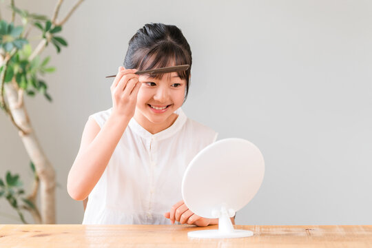 A girl, elementary school or middle school student, styling her hair while looking in the mirror.