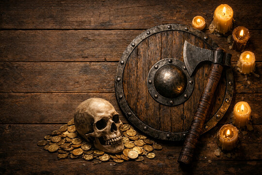Viking warrior equipment with wooden shield, battle axe, skull, gold coins and burning candles arranged on rustic wooden table creating dramatic medieval still life.