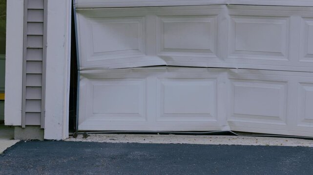 Damaged residential garage door with bent panels after vehicle impact or structural accident. Exterior home damage illustrating repair, insurance, maintenance, and property restoration.