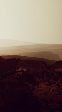 The scene shows a vast desert with hills and distant mountains. The light of sunset creates shadows and highlights on the ground. The area appears dry with few plants.