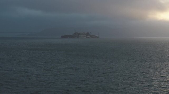 Sunset peeking through storm clouds onto sparkling, choppy waves of San Francisco bay near alcatraz island - wide, aerial shot