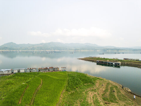 Aerial view of Wadaslintang Reservoir with floating fish farms, lush green terraced fields, and distant hills in Wadaslintang, Central Java, Indonesia.