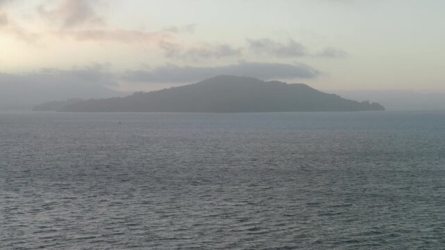 Swooping drone shot over choppy waves in San Francisco bay with view of silhouetted hill ahead