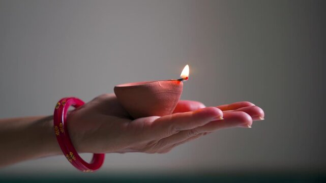 Closeup shot of hand on an Indian woman wearing bangles holding Diya oil lamp in her hand during the Diwali festival in India. Deepavali festival background with copy space. Female holds diya in hand.