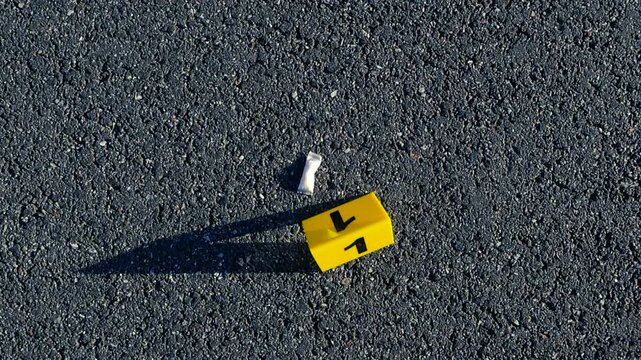 Yellow crime scene evidence marker with the number one next to a small white bag containing a tobacco free nicotine pouch on an asphalt road during an investigation, with a blurry background