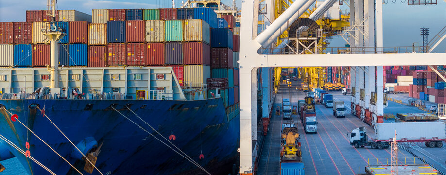 gantry cranes loading cargo container ship at a busy commercial port terminal, with trailer trucks lined up on the dock to support global maritime logistics and supply chain operations.