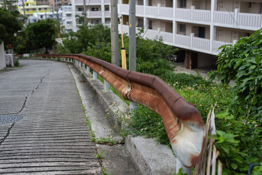 坂道に設置された一部がぶつけられて変形している錆びたガードレール