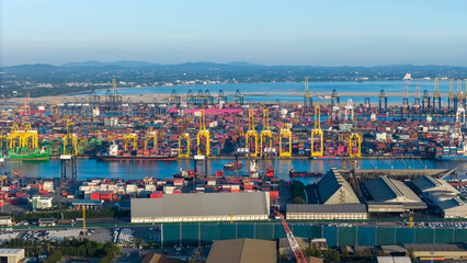 Obraz premium commercial port terminal with cargo ships, container stacks, gantry cranes, storage warehouses, and large car parking lots facilitating global maritime trade and logistics supply chain.