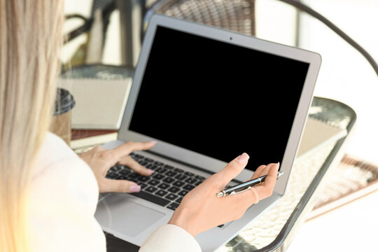 Woman using laptop with pen in hand at glass table