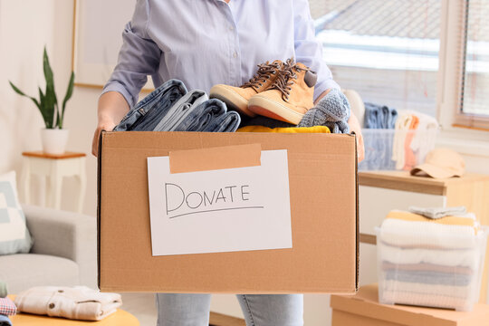Person holding a donation box filled with clothes and shoes