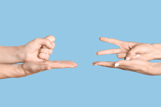 Hands playing rock paper scissors game on blue background