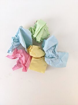 Crumpled colorful paper ball symbolizing creativity, recycling and discarded ideas on plain white background.