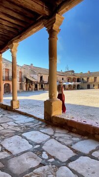 Back view of female tourist discovers historic medieval town square looking at old stone buildings in Spain, Paza Mayor of Pedraza