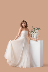 Fototapeta premium Beautiful bride in wedding dress with flowers on beige background