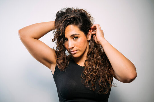 Confident young adult woman touching curly brown hair