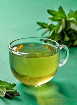 Glass cup of fresh mint tea with mint leaves on green background