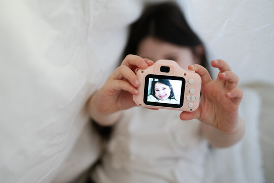 Taking a smiling selfie with a pink toy camera under a white blanket