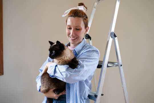 Woman holding a Siamese cat indoors during home renovation