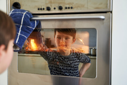 Mirror image of proud boy watching cake in oven