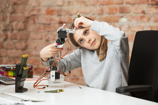 Girl with work tool building robotic arm at table