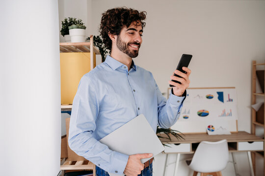 Happy young engineer using mobile phone and holding smart phone at office