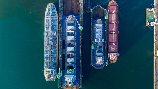 commercial cargo ships and heavy oil tankers undergoing essential maintenance and structural repairs inside floating dry docks at a busy industrial shipyard marine facility.