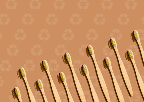 Pattern of wooden toothbrushes flat laid against brown background with recycling symbols