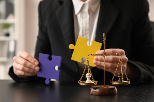 Pawns on justice scales against mediator with puzzle pieces at table in office, closeup