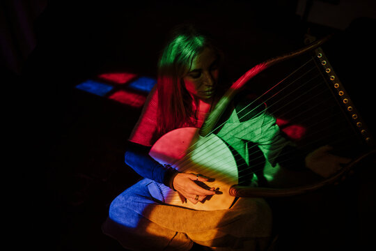 Musician playing a lyre in the dark with colorful abstract lighting