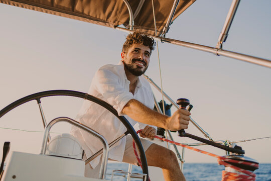 Sailor steering a sailboat on the ocean during summer vacation