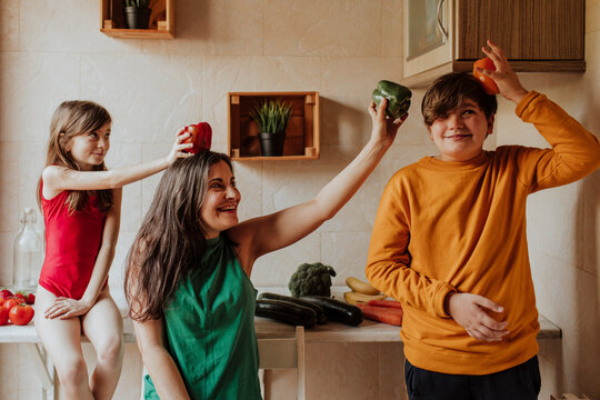 Mother and children playing with vegetables in kitchen