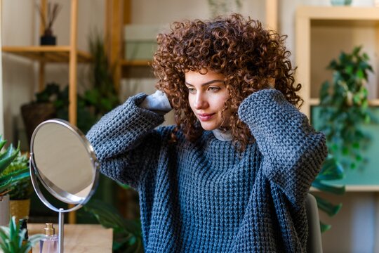 Woman adjusting curly hair in mirror at home for morning self-care