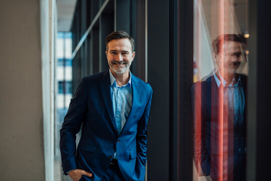 Smiling businessman standing with hand in pocket near window