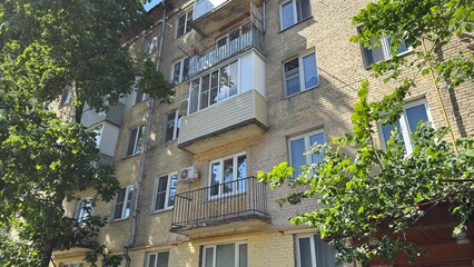 Brick apartment building with balconies and green trees in sunny urban residential neighborhood © belavinstock