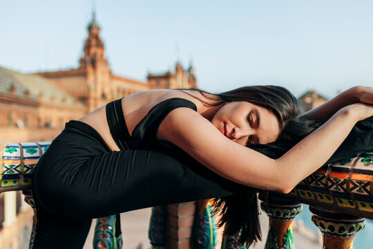Ballet dancer with eyes closed leaning over stretched leg on railing