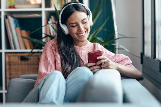 Smiling user relaxing on cozy sofa listening to music on cell phone
