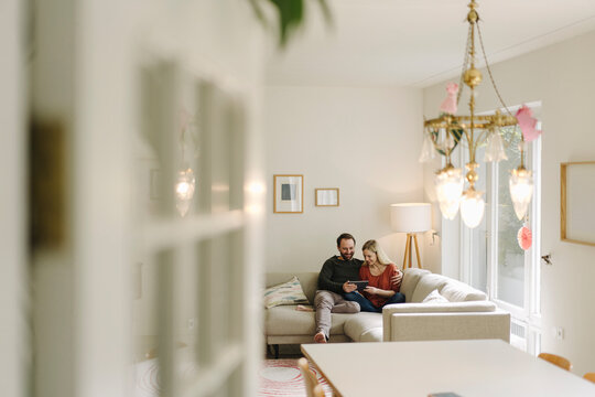 Couple sitting at home on couch, using digital tablet