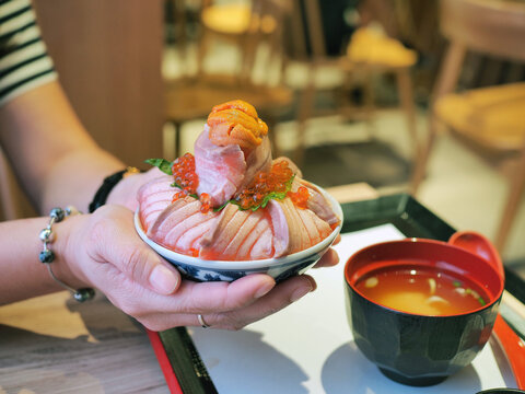 Bowl of loaded sliced grilled Salmon or aburi sashimi top with salmon roe, fresh uni and oba leaf.