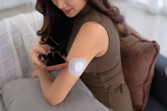 Asian female living at home with continuous glucose monitor patch for diabetes management, CGM