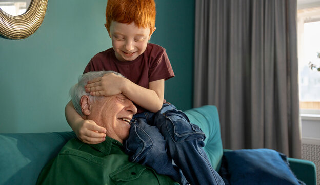 Smiling grandfather and grandson playing on sofa at home