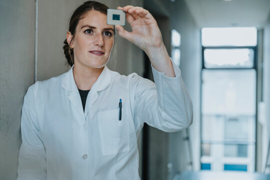 Female scientist holding computer chip while leaning on wall at clinic