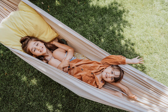 Smiling sister and brother lying in hammock at back yard