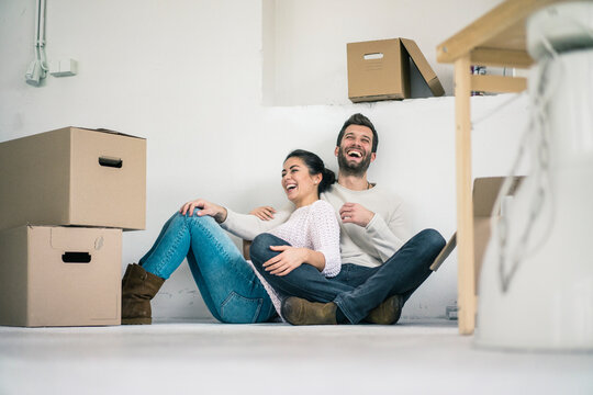 Laughing couple sitting in new home surrounded by cardboard boxes
