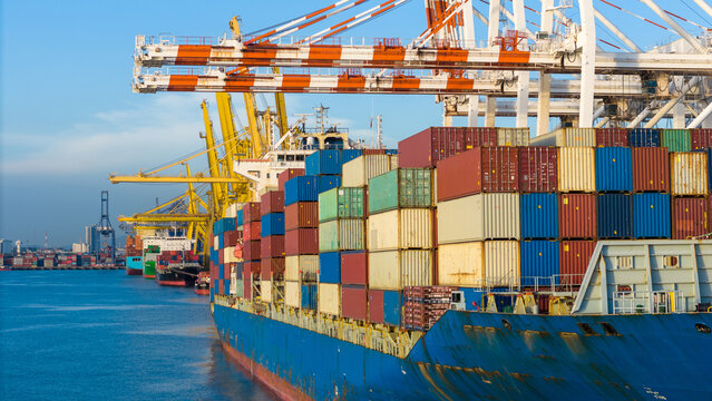cargo container ship docked at a commercial port terminal with giant gantry cranes loading freight, representing global maritime logistics, supply chain, and international trade.